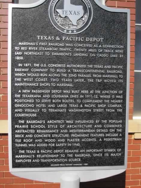Historical Marker about the Texas & Pacific (T&P) Depot in Marshall Texas ... Marshall's first railroad was conceived as a connection to Red River steamboat traffic. Twenty miles of track were laid northeast to Swanson's Landing on Caddo Lake by 1858. In 1871, the U. S. Congress authorized the Texas & Pacific Railway Company to build a transcontinental railroad, which would run along the 32nd parallel from Marshall to the West Coast. Two years later, the T&P moved its maintenance shops to Marshall. A new passenger depot was built here at the junction of the Texarkana and Louisiana lines in 1911-12, where it was positioned to serve both routes. To complement the nearby Ginocchio Hotel and huge Texas & Pacific shop complex, and visually to terminate Washington Street from the Courthouse. The railroad's architect was influenced by the popular prairie school and combined abstracted renaissance and Mediterranean details on the brick and concrete structure. Prominent features include a tile roof and wood and plaster accents. A pedestrian tunnel was added for safety in 1940. The Texas & Pacific depot remains an important symbol of Marshall's relationship to the railroad, once its major employer and transportation source. Recorded Texas Historic Landmark - 1985